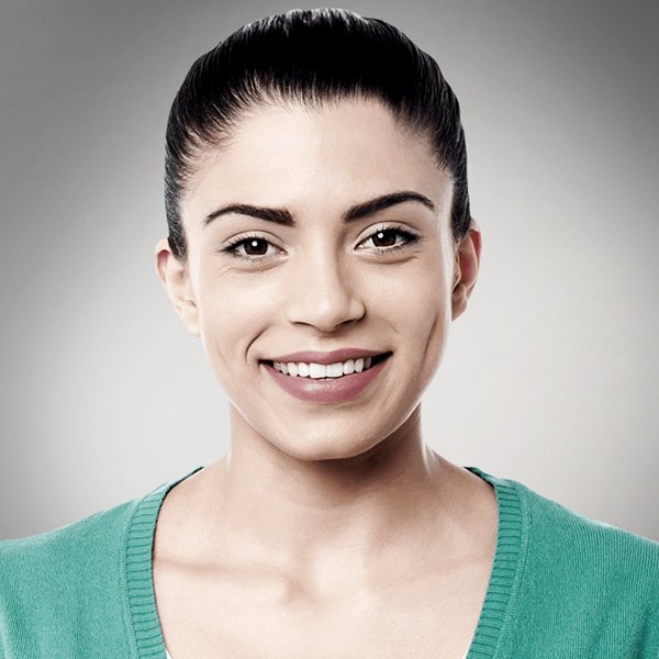 Smiling woman with dark hair in a teal sweater against a light gray background