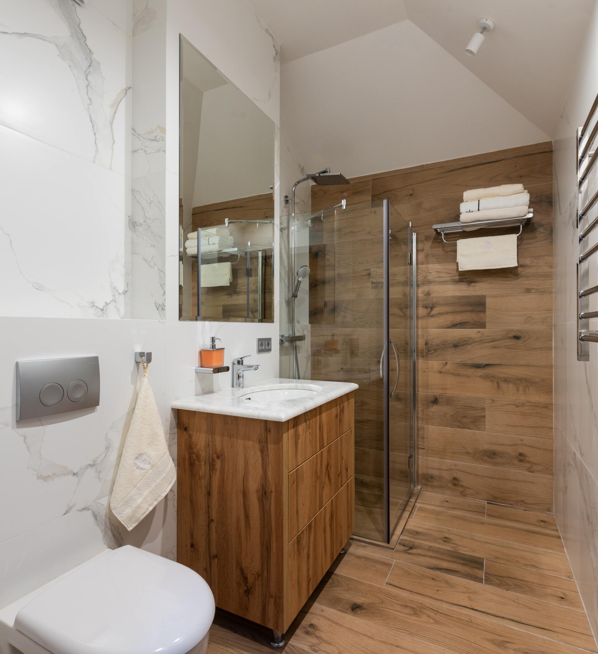 Modern bathroom with marble walls, wood vanity, glass shower, and towel rack