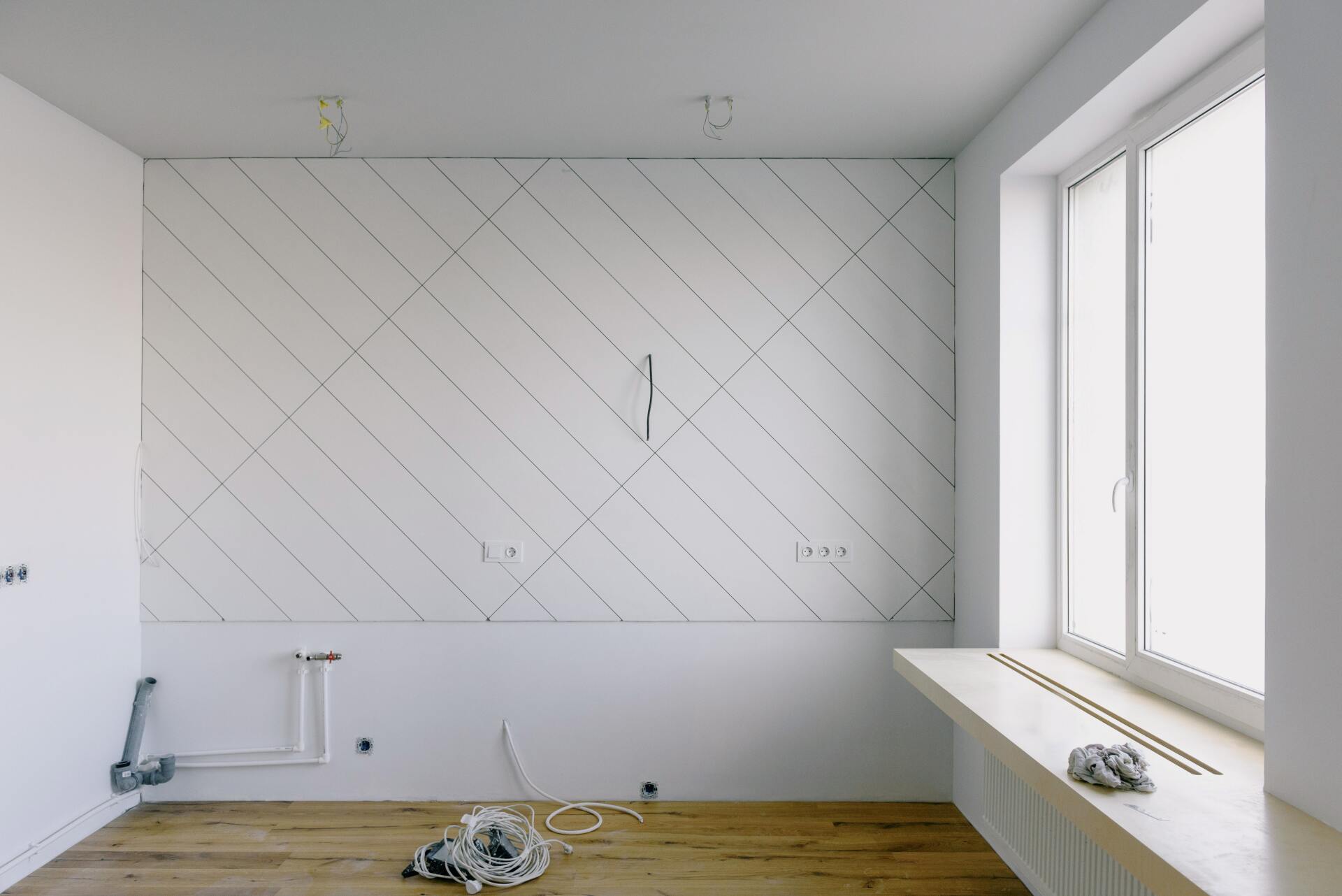 Empty white room with diagonal wall paneling, wood floor, and large windows on the right.