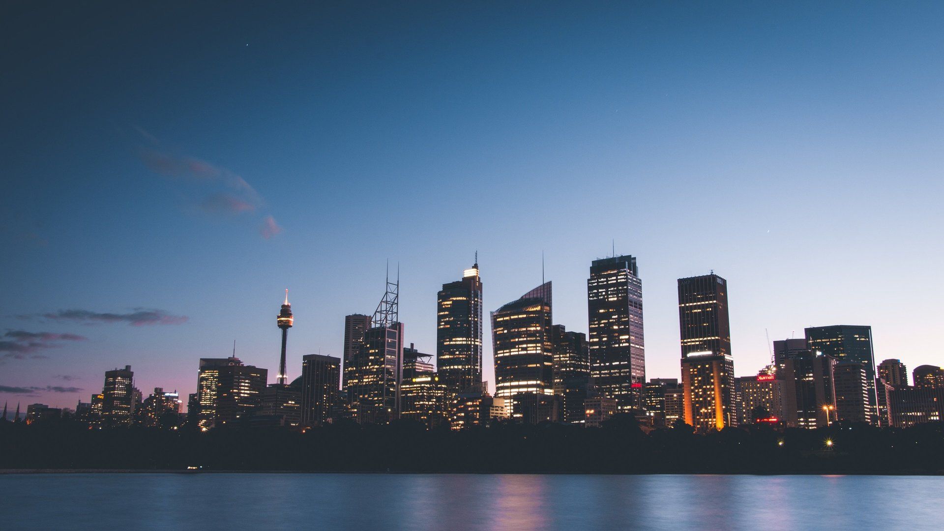 City skyline at dusk with illuminated skyscrapers reflected on calm water under a blue-pink sky