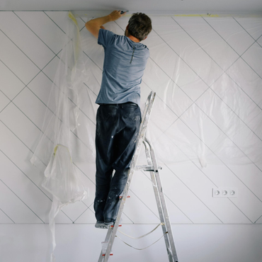 Person on a ladder painting a white wall with diagonal guide lines