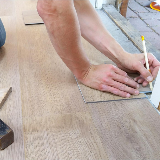 Hands marking measurements on a wooden board with a pencil outdoors.